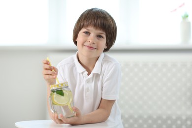 Photo of Cute little boy with mason jar of lemonade at table indoors. Refreshing drink