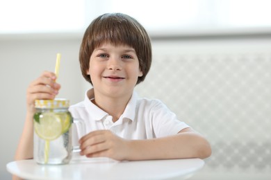 Photo of Cute little boy with mason jar of lemonade at table indoors. Refreshing drink
