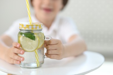 Photo of Little boy with mason jar of lemonade at table indoors, selective focus. Refreshing drink