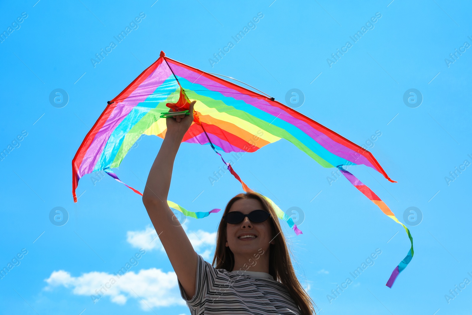 Woman with colorful kite under blue sky, low angle view Photo of Woman with colorful kite under blue sky, low angle view