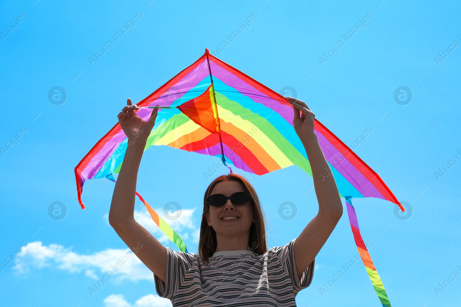 Woman with colorful kite under blue sky, low angle view Photo of Woman with colorful kite under blue sky, low angle view