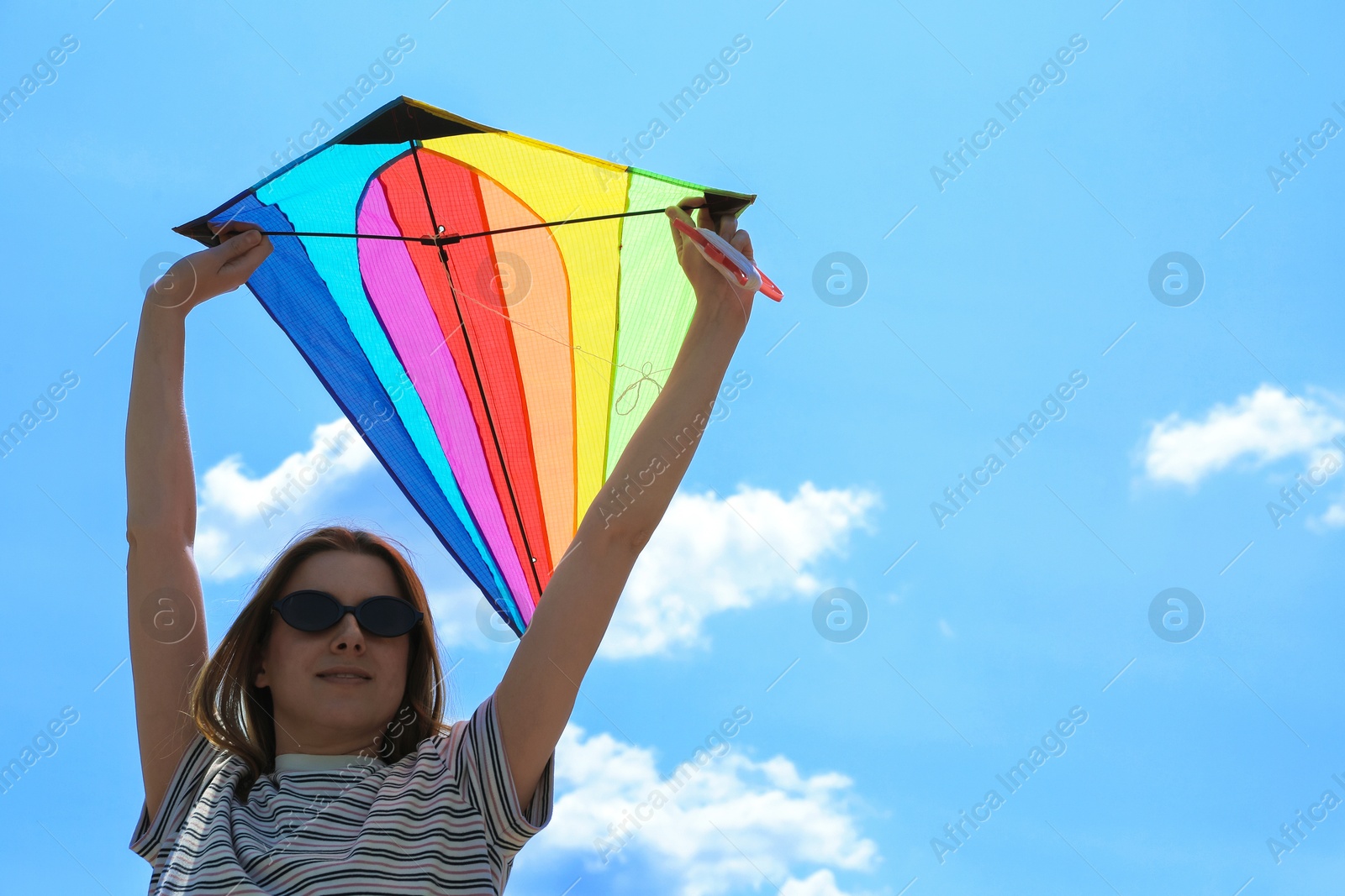 Woman with colorful kite under blue sky, low angle view Photo of Woman with colorful kite under blue sky, low angle view