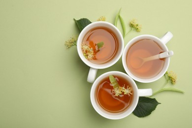 Photo of Tasty linden tea in cups, spoon, leaves and flowers on light green background, flat lay. Space for text