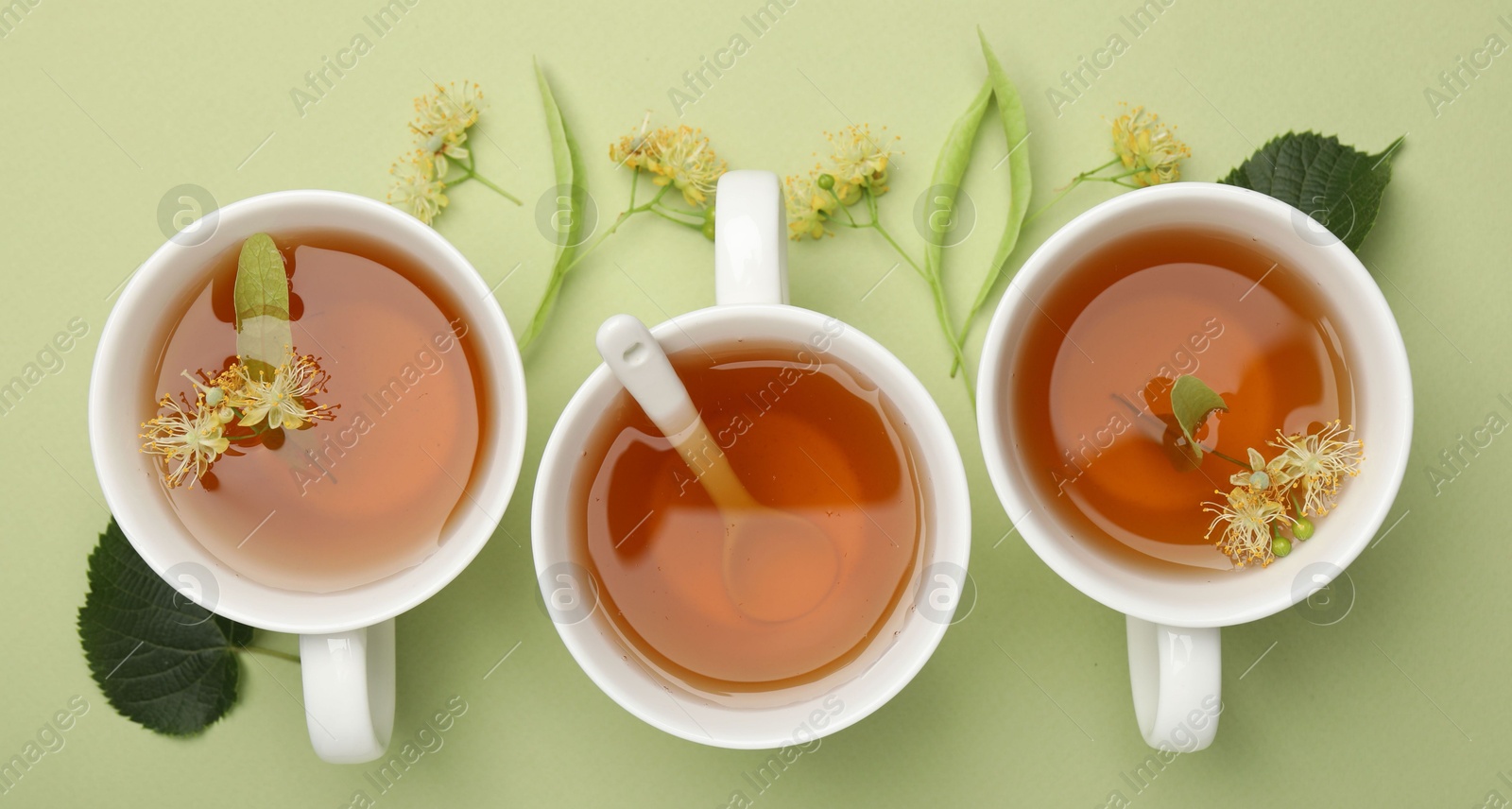 Tasty linden tea in cups, spoon, leaves and flowers on light green background, flat lay Photo of Tasty linden tea in cups, spoon, leaves and flowers on light green background, flat lay