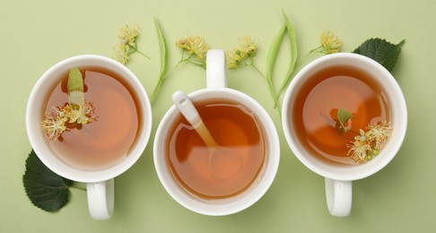 Photo of Tasty linden tea in cups, spoon, leaves and flowers on light green background, flat lay