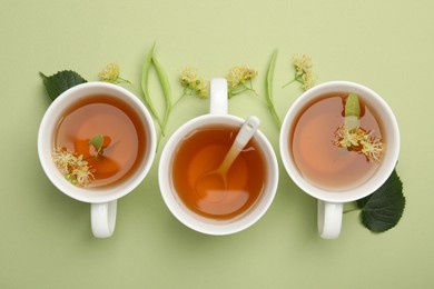 Photo of Tasty linden tea in cups, spoon, leaves and flowers on light green background, flat lay