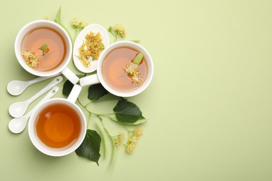 Photo of Tasty linden tea in cups, spoons, leaves and flowers on light green background, flat lay. Space for text