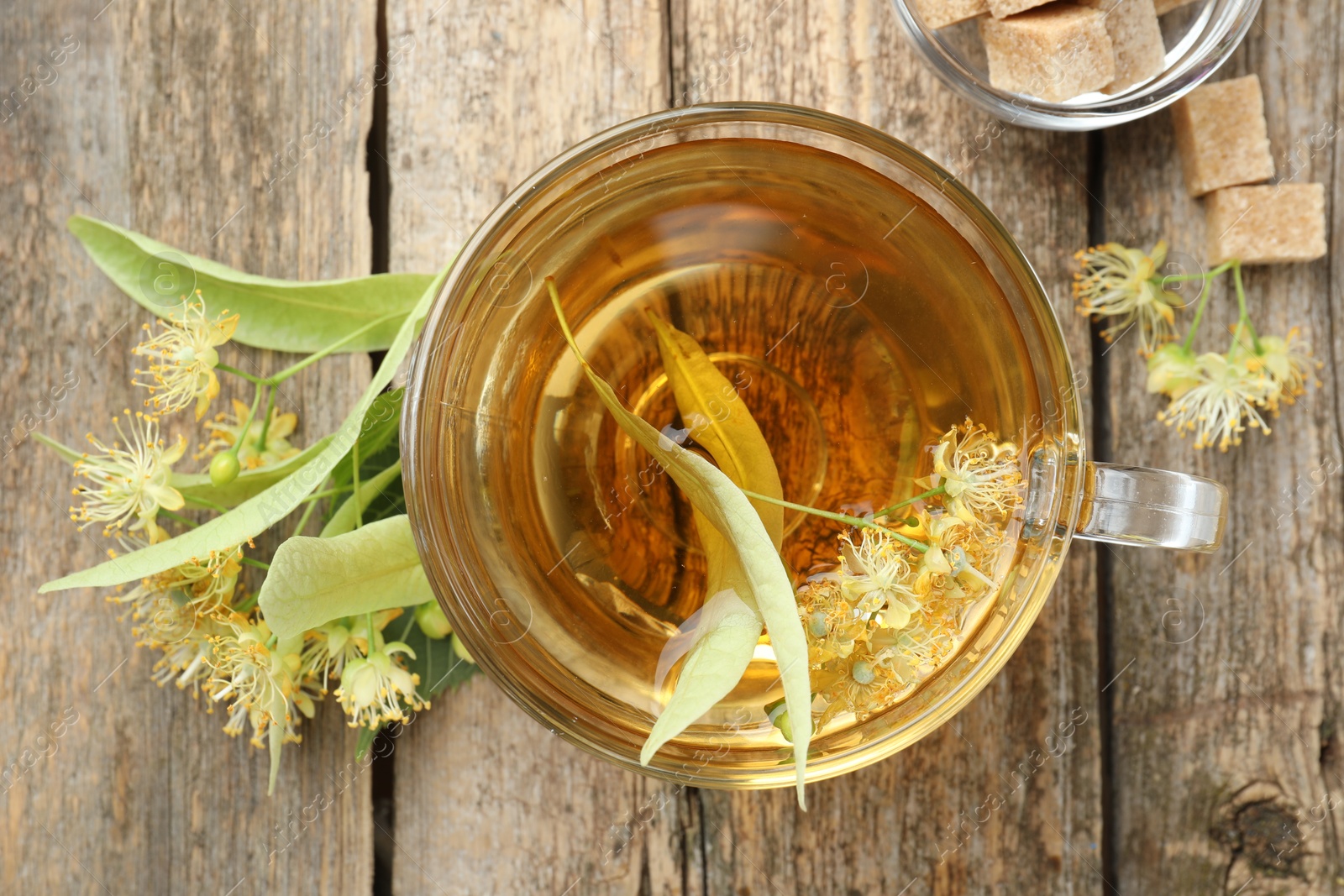 Tasty linden tea in cup, sugar cubes, leaves and flowers on wooden table, flat lay Photo of Tasty linden tea in cup, sugar cubes, leaves and flowers on wooden table, flat lay