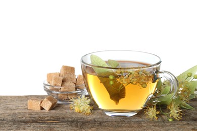 Photo of Tasty linden tea in cup, sugar cubes, leaves and flowers on wooden table against white background