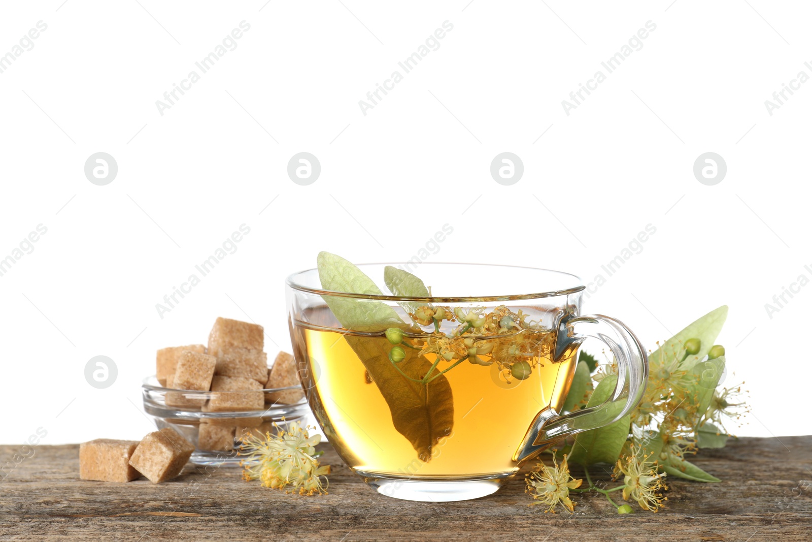 Tasty linden tea in cup, sugar cubes, leaves and flowers on wooden table against white background Photo of Tasty linden tea in cup, sugar cubes, leaves and flowers on wooden table against white background