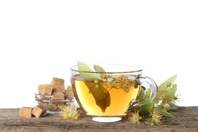 Photo of Tasty linden tea in cup, sugar cubes, leaves and flowers on wooden table against white background