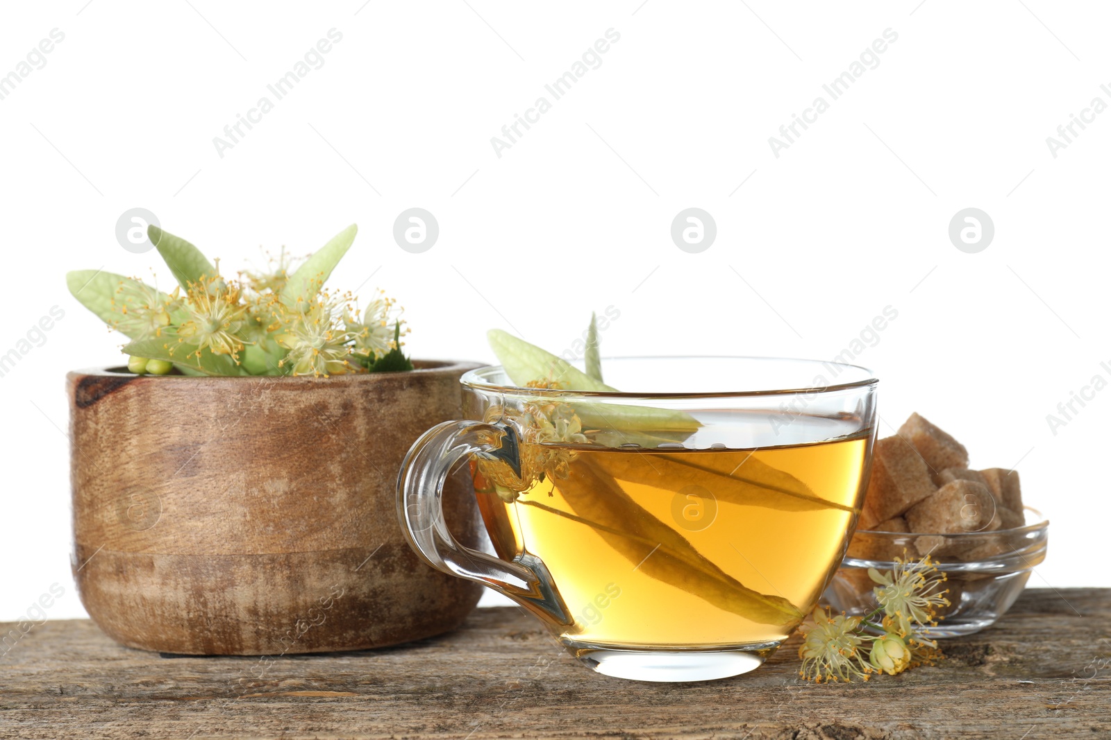 Tasty linden tea in cup, sugar cubes, leaves and flowers on wooden table against white background Photo of Tasty linden tea in cup, sugar cubes, leaves and flowers on wooden table against white background