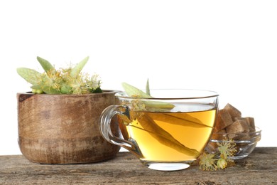 Photo of Tasty linden tea in cup, sugar cubes, leaves and flowers on wooden table against white background