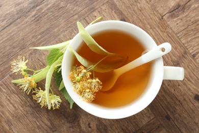 Photo of Tasty linden tea in cup, leaves and flowers on wooden table, flat lay