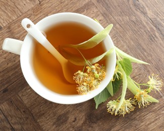 Photo of Tasty linden tea in cup, leaves and flowers on wooden table, flat lay