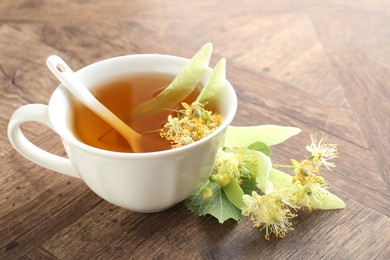 Photo of Tasty linden tea in cup, leaves and flowers on wooden table, closeup