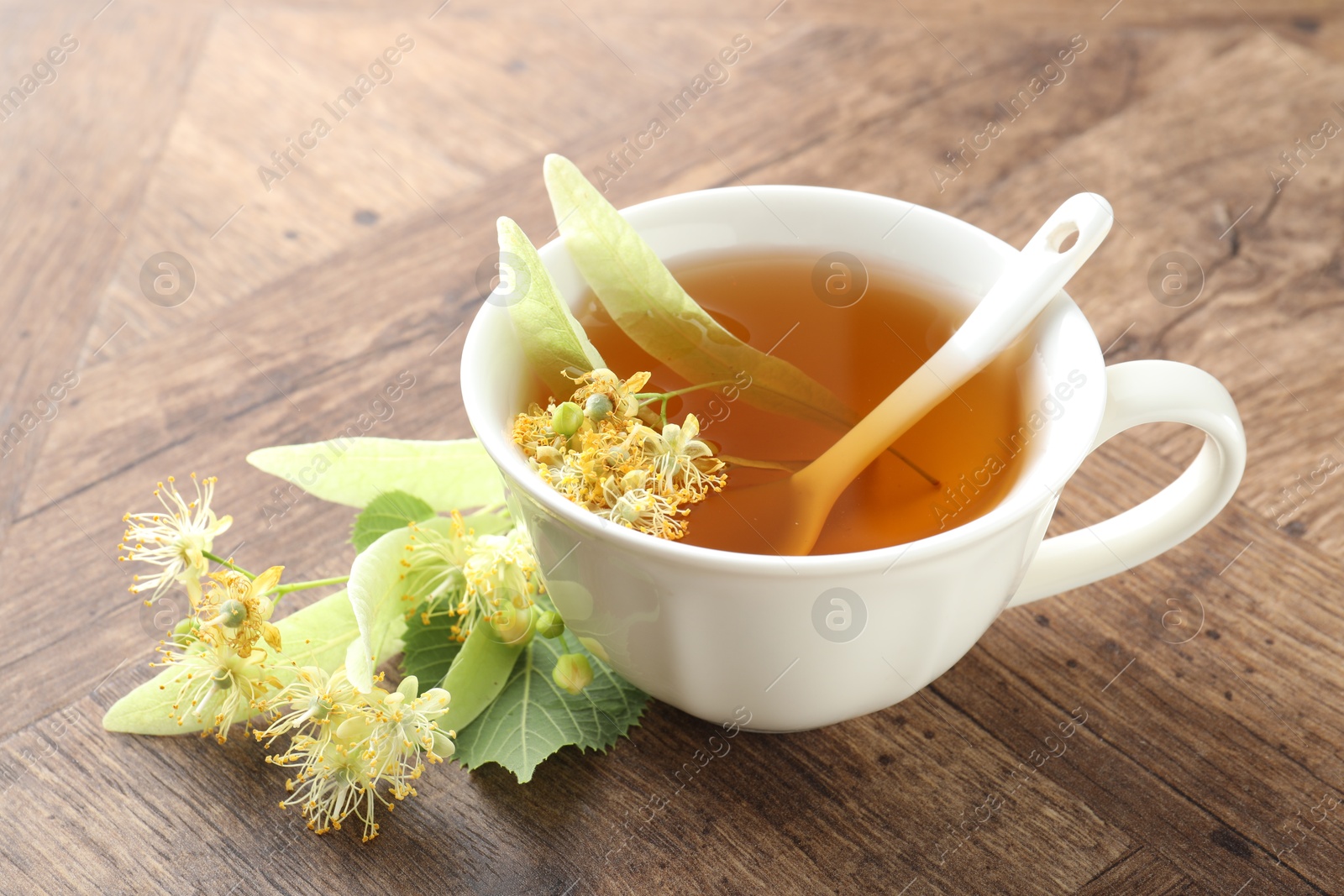 Tasty linden tea in cup, leaves and flowers on wooden table, closeup Photo of Tasty linden tea in cup, leaves and flowers on wooden table, closeup