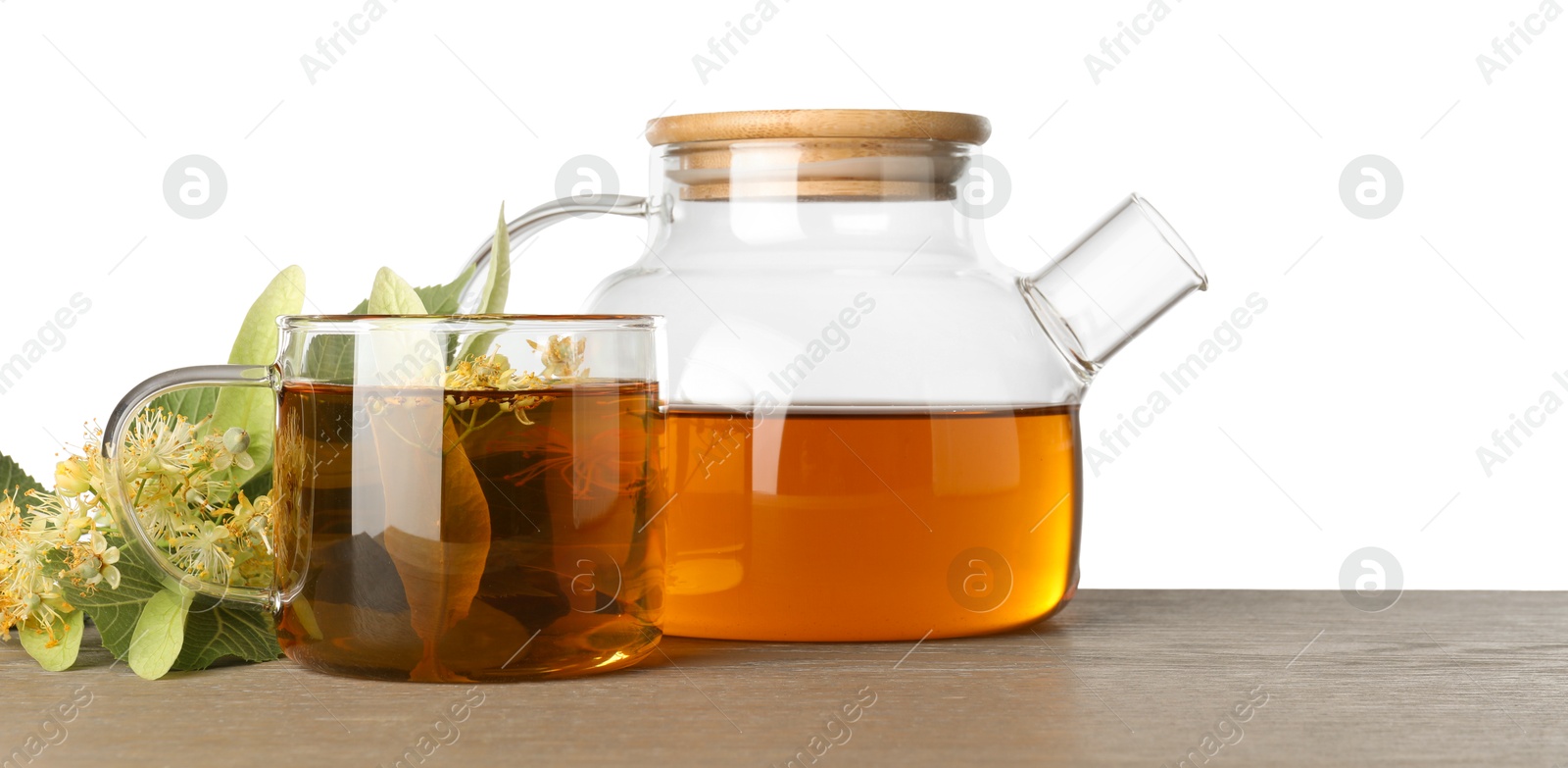 Photo of Tasty linden tea in cup, teapot, leaves and flowers on wooden table against white background