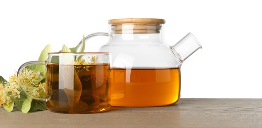 Photo of Tasty linden tea in cup, teapot, leaves and flowers on wooden table against white background