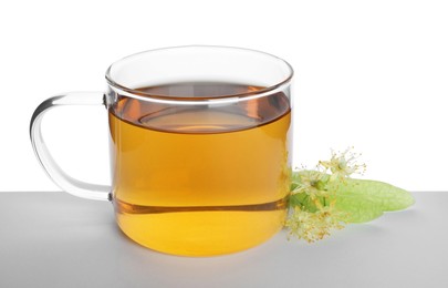 Photo of Tasty linden tea in cup, leaves and flowers on table against white background