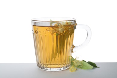 Photo of Tasty linden tea in cup, leaves and flowers isolated on white
