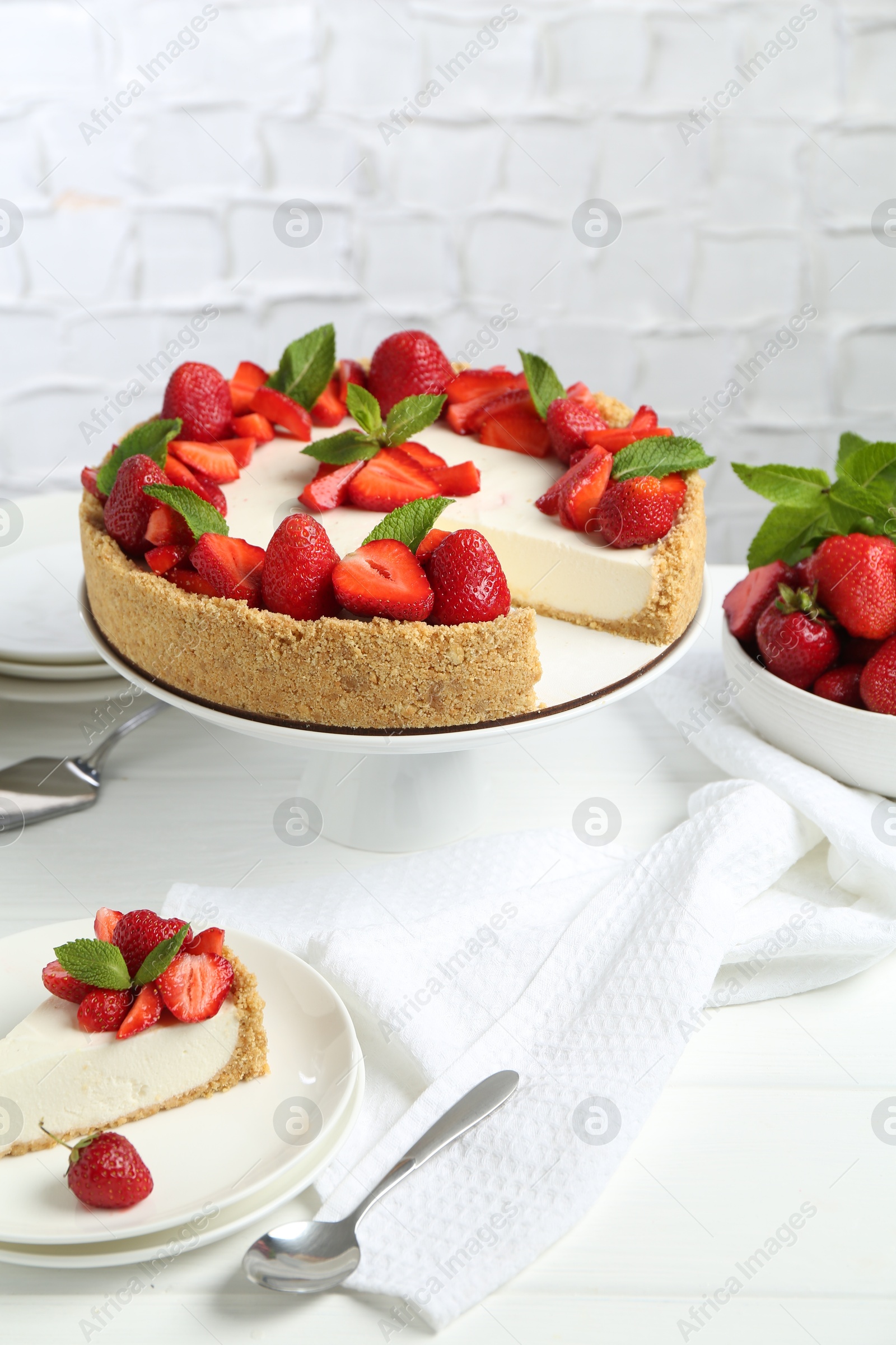 Photo of Delicious cheesecake with strawberries and mint on white wooden table