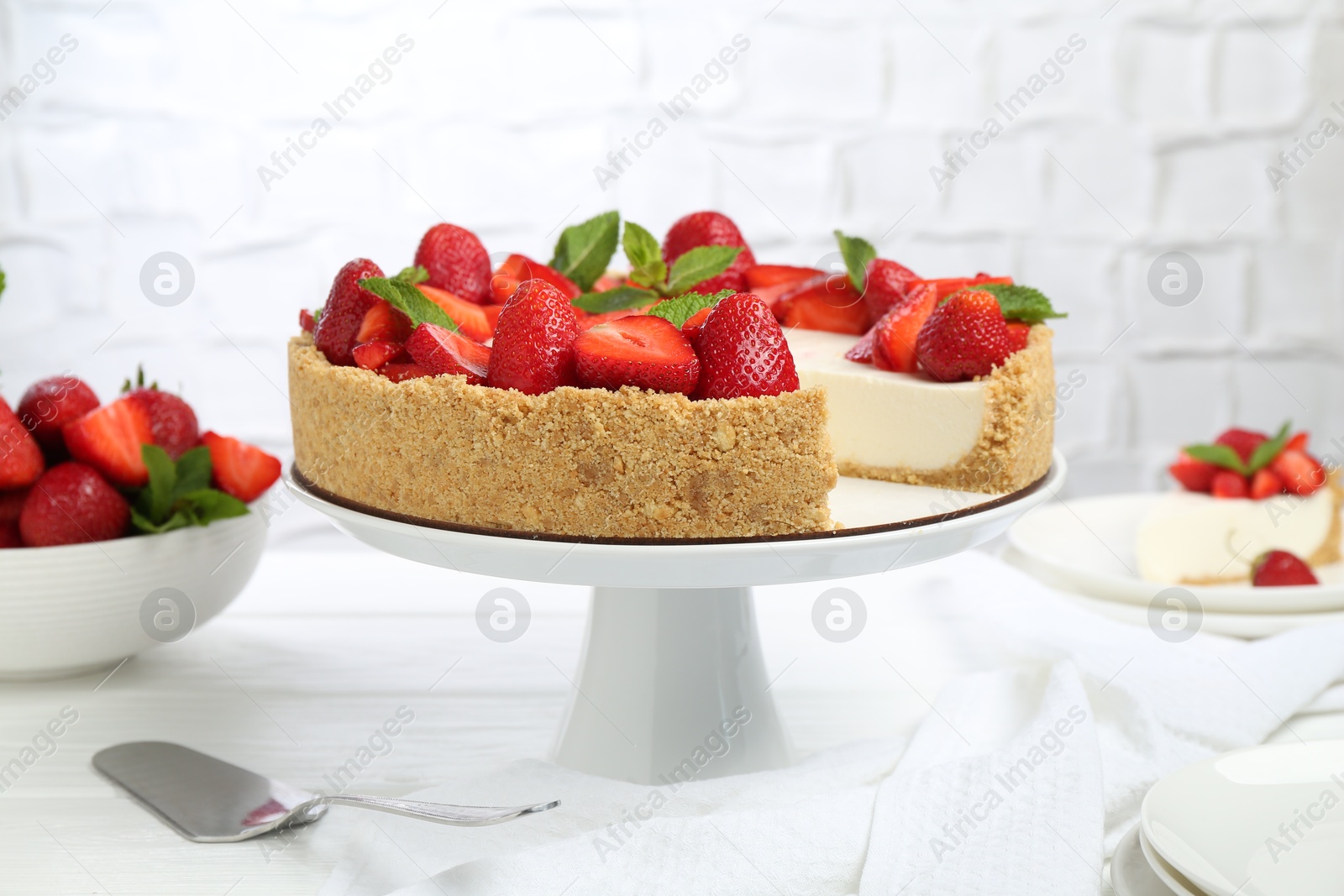 Photo of Delicious cheesecake with strawberries and mint on white wooden table, closeup