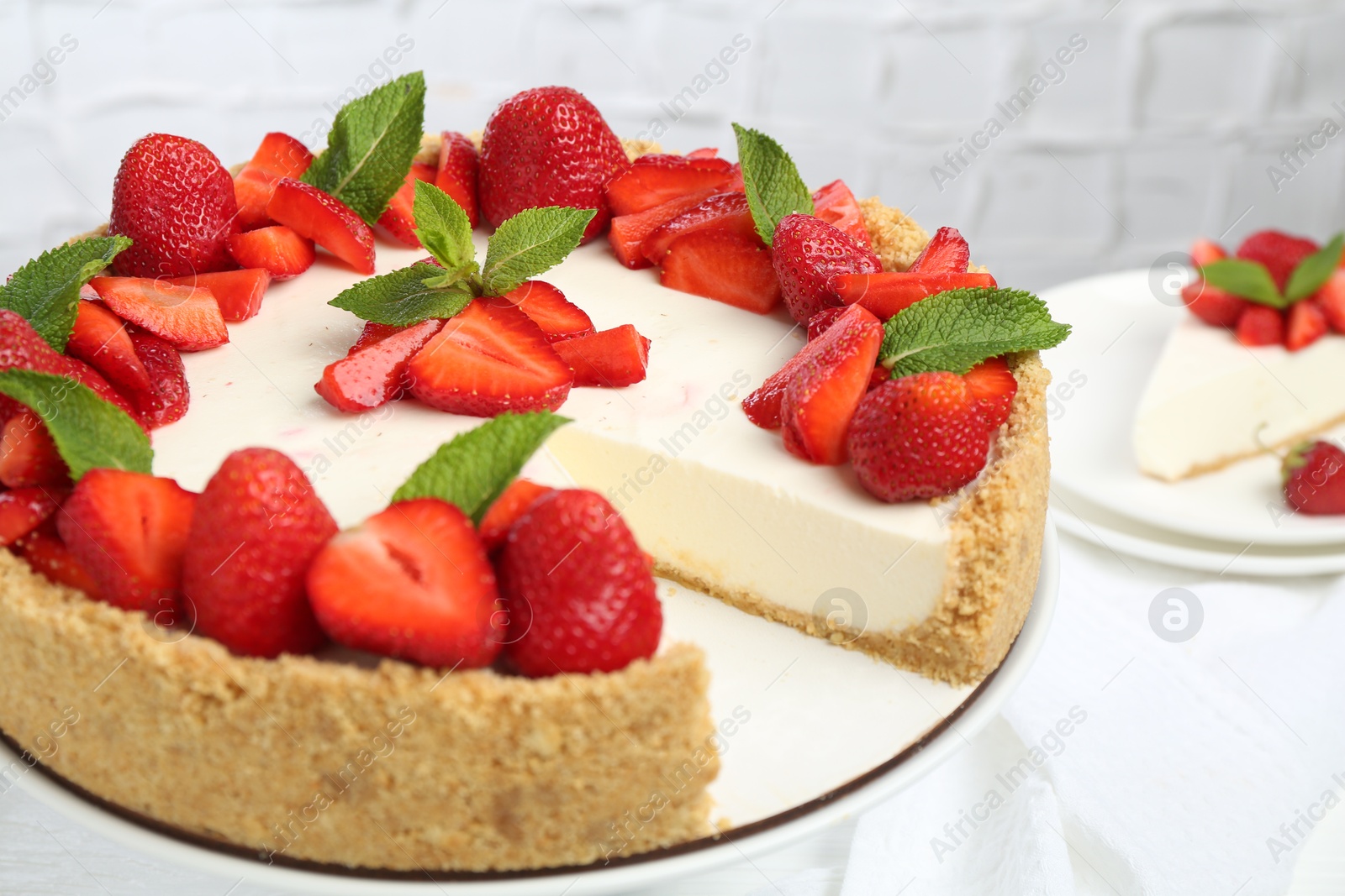 Photo of Delicious cheesecake with strawberries and mint on table, closeup