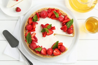 Photo of Delicious cheesecake with strawberries, mint, server and tea on white wooden table, flat lay