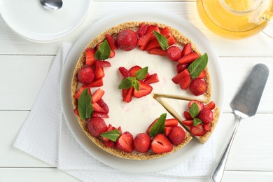Photo of Delicious cheesecake with strawberries, mint, server and tea on white wooden table, flat lay