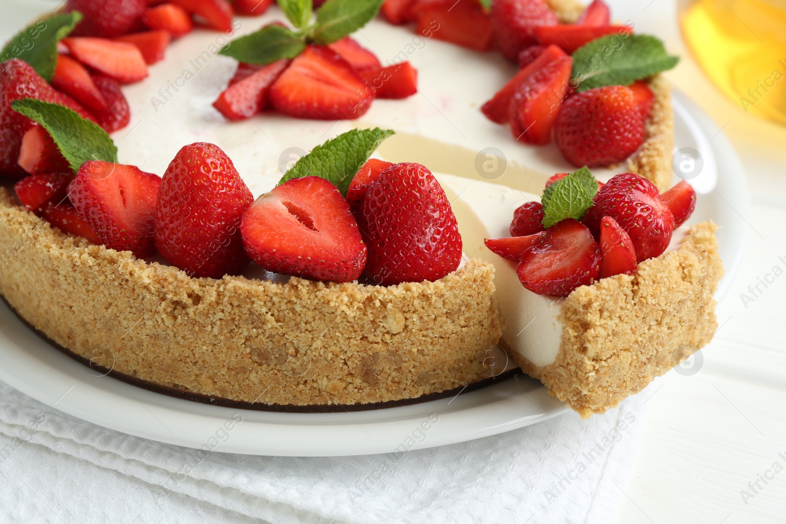 Photo of Delicious cheesecake with strawberries and mint on white table, closeup