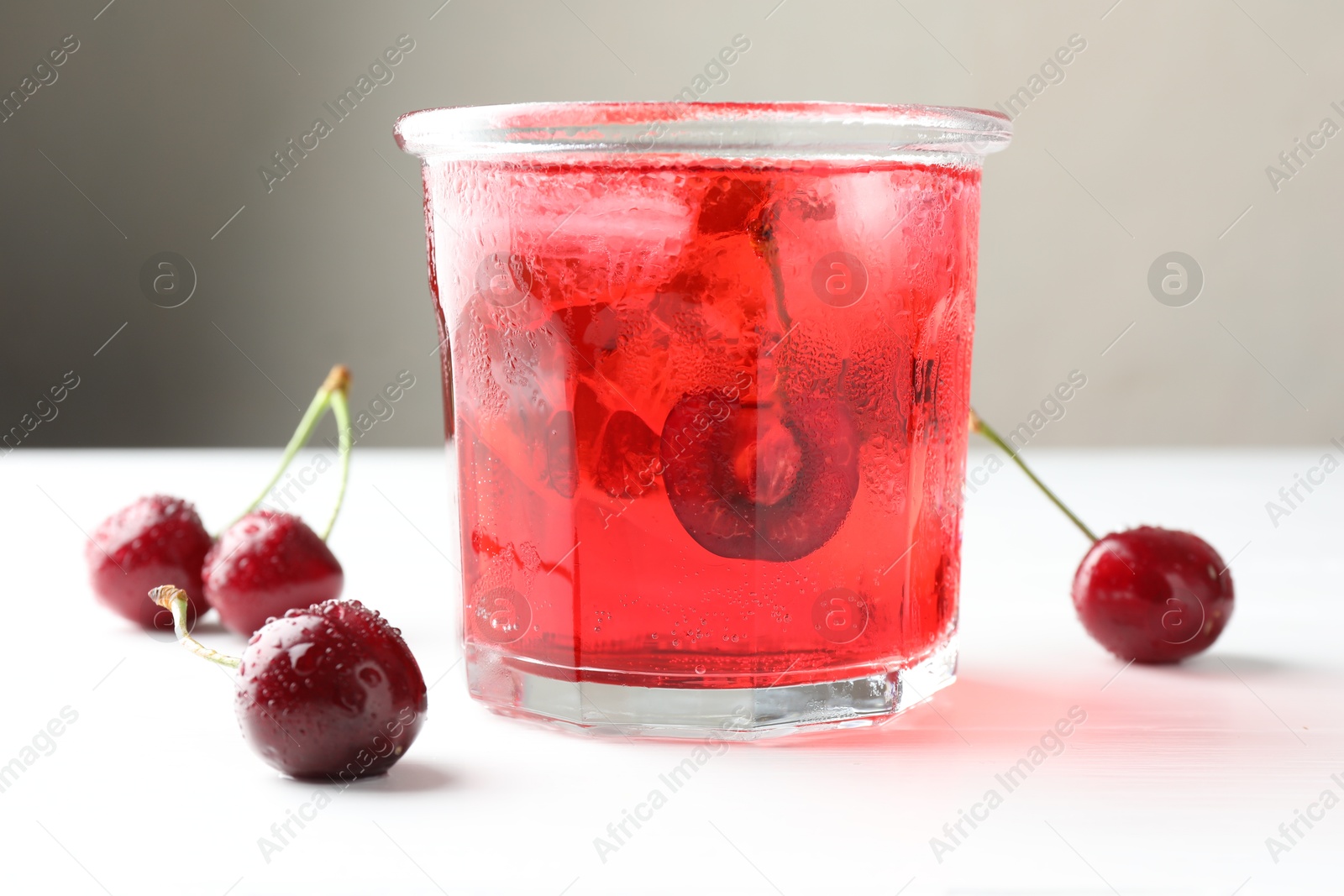 Tasty cherry soda with ice cubes and berries on white wooden table, closeup Photo of Tasty cherry soda with ice cubes and berries on white wooden table, closeup