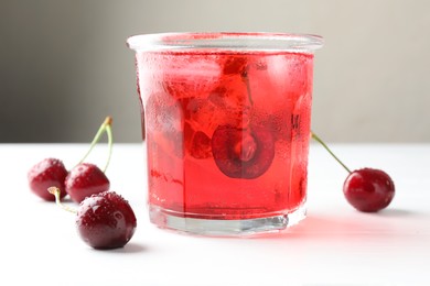 Photo of Tasty cherry soda with ice cubes and berries on white wooden table, closeup