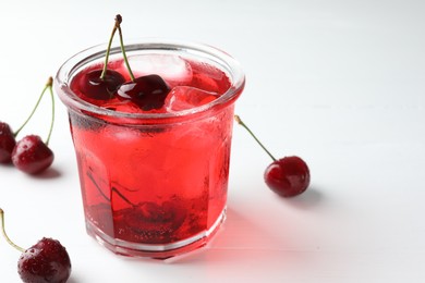 Photo of Tasty cherry soda with ice cubes and berries on white wooden table, closeup. Space for text