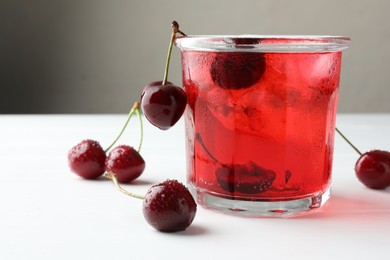 Photo of Tasty cherry soda with ice cubes and berries on white wooden table, closeup