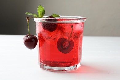 Photo of Tasty cherry soda with ice cubes, mint and berries on white wooden table, closeup