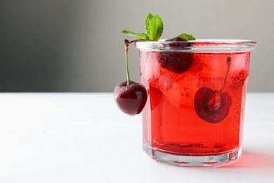 Photo of Tasty cherry soda with ice cubes, mint and berries on white wooden table, closeup. Space for text