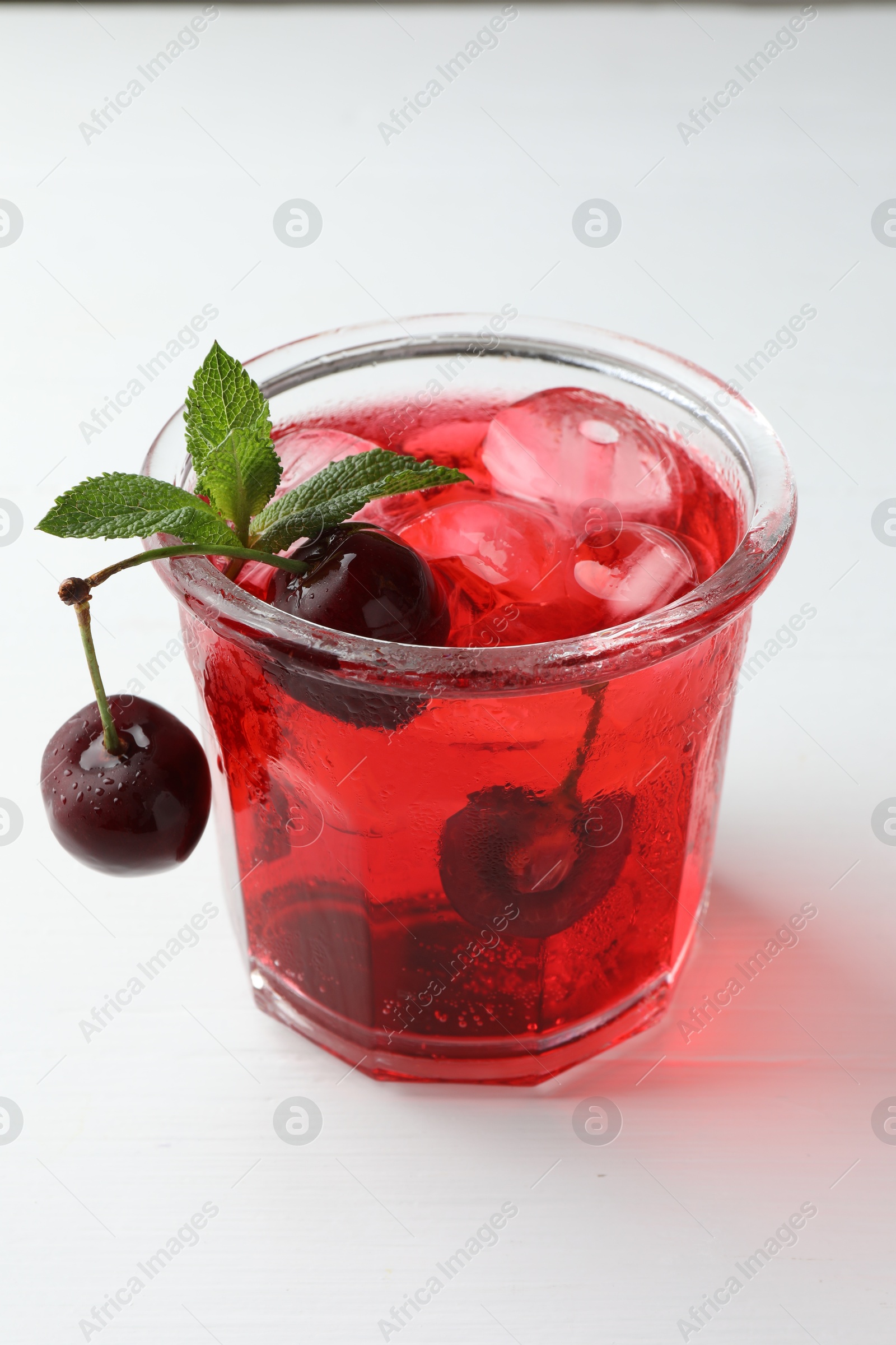 Tasty cherry soda with ice cubes, mint and berries on white wooden table, closeup Photo of Tasty cherry soda with ice cubes, mint and berries on white wooden table, closeup