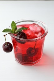 Photo of Tasty cherry soda with ice cubes, mint and berries on white wooden table, closeup