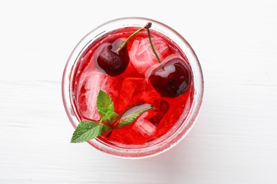 Photo of Tasty cherry soda with ice cubes, mint and berries on white wooden table, top view