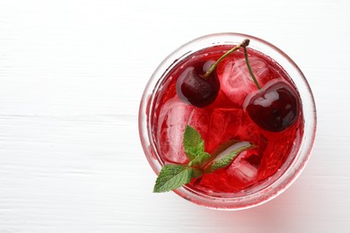 Photo of Tasty cherry soda with ice cubes, mint and berries on white wooden table, top view. Space for text