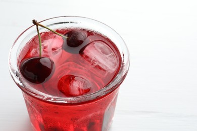 Photo of Tasty cherry soda with ice cubes and berries on white wooden table, closeup. Space for text