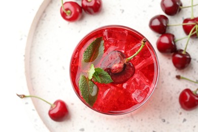 Photo of Tasty cherry soda with ice cubes, mint and berries on white table, flat lay