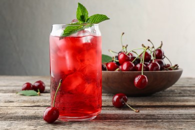 Photo of Tasty cherry soda with ice cubes, berries and mint on wooden table, closeup