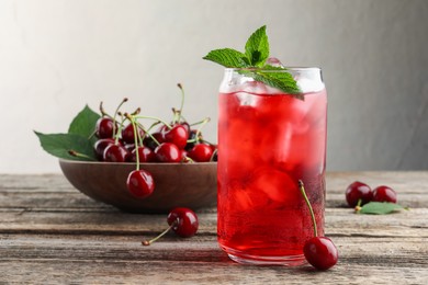 Photo of Tasty cherry soda with ice cubes, berries and mint on wooden table, closeup