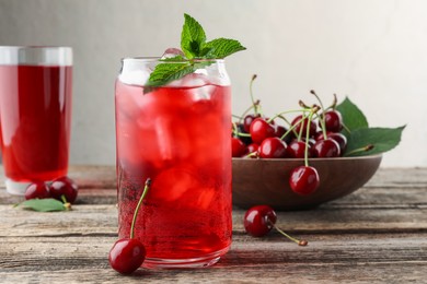 Photo of Tasty cherry soda with ice cubes, berries and mint on wooden table, closeup