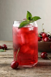 Photo of Tasty cherry soda with ice cubes, berries and mint on wooden table, closeup