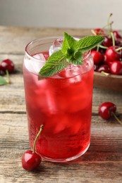 Photo of Tasty cherry soda with ice cubes, berries and mint on wooden table, closeup