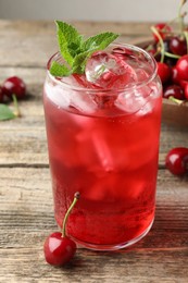 Photo of Tasty cherry soda with ice cubes, berries and mint on wooden table, closeup