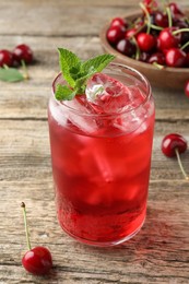 Photo of Tasty cherry soda with ice cubes, berries and mint on wooden table, closeup